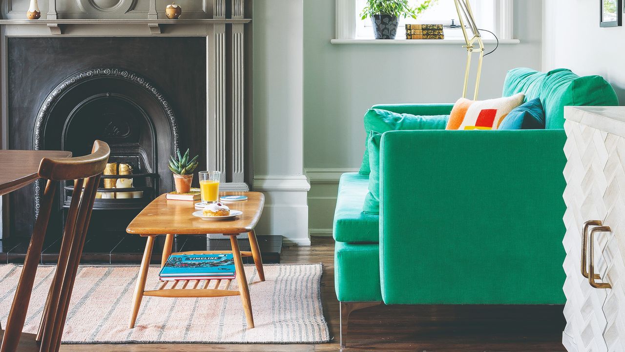 A living room with a bright green sofa and a striped rug with a wooden mid-century modern coffee table on top