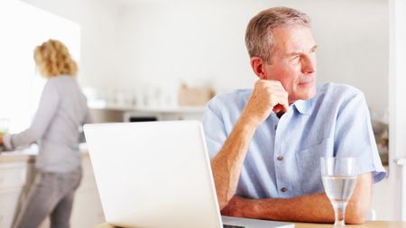 Thoughtful man with laptop while woman cooking in kitchen 