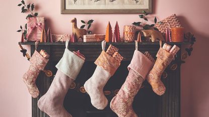 A fireplace set against a pink wall with pink Christmas stockings and decor, including a garland made with dried orange slices