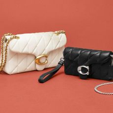 A cream and a black bag from Coach in front of a red backdrop.