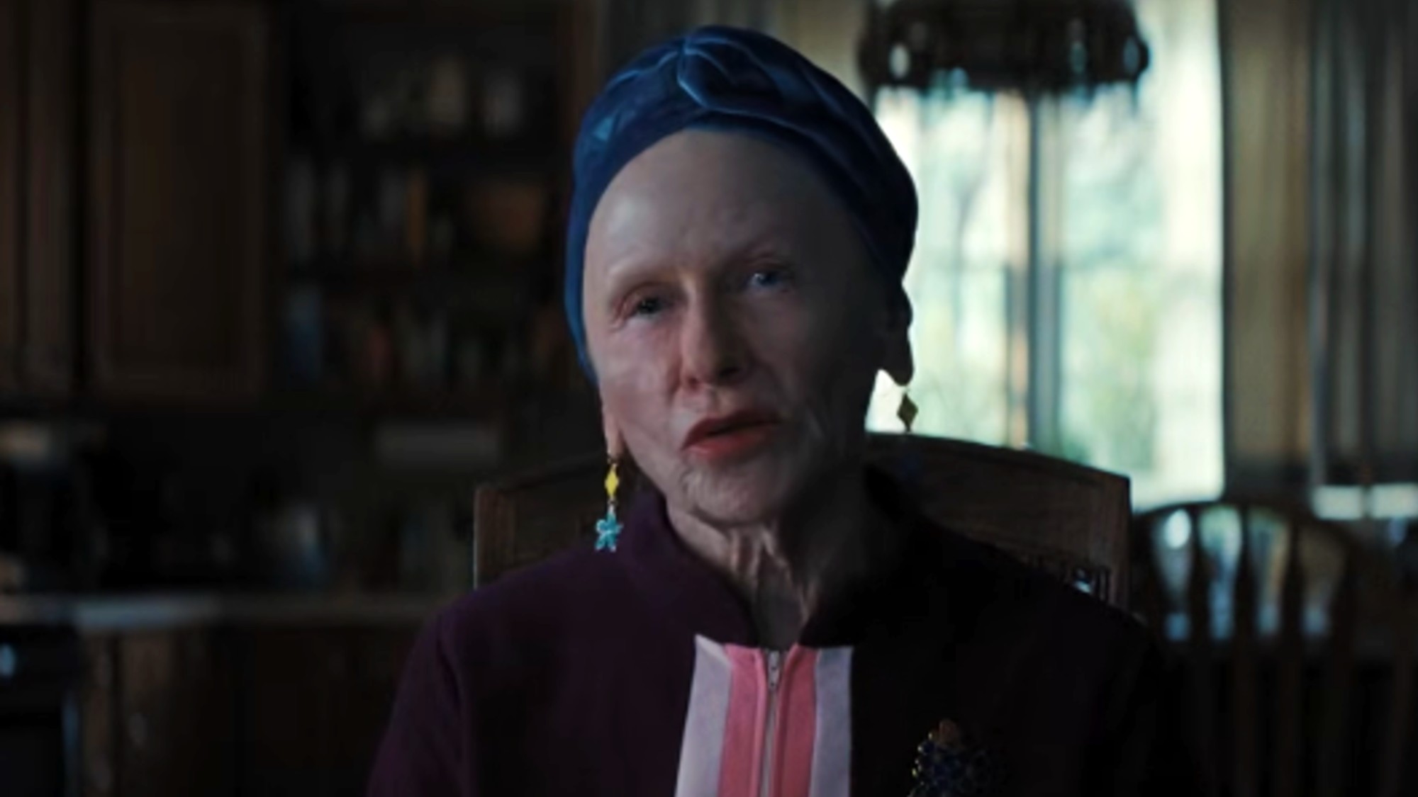 Amy Madigan with a blue head scarf, sitting at a dining room table in Weapons
