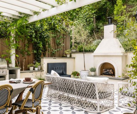 An outdoor living area with a large fireplace, patterned floor tiles, a water feature, and furniture with a knotted design