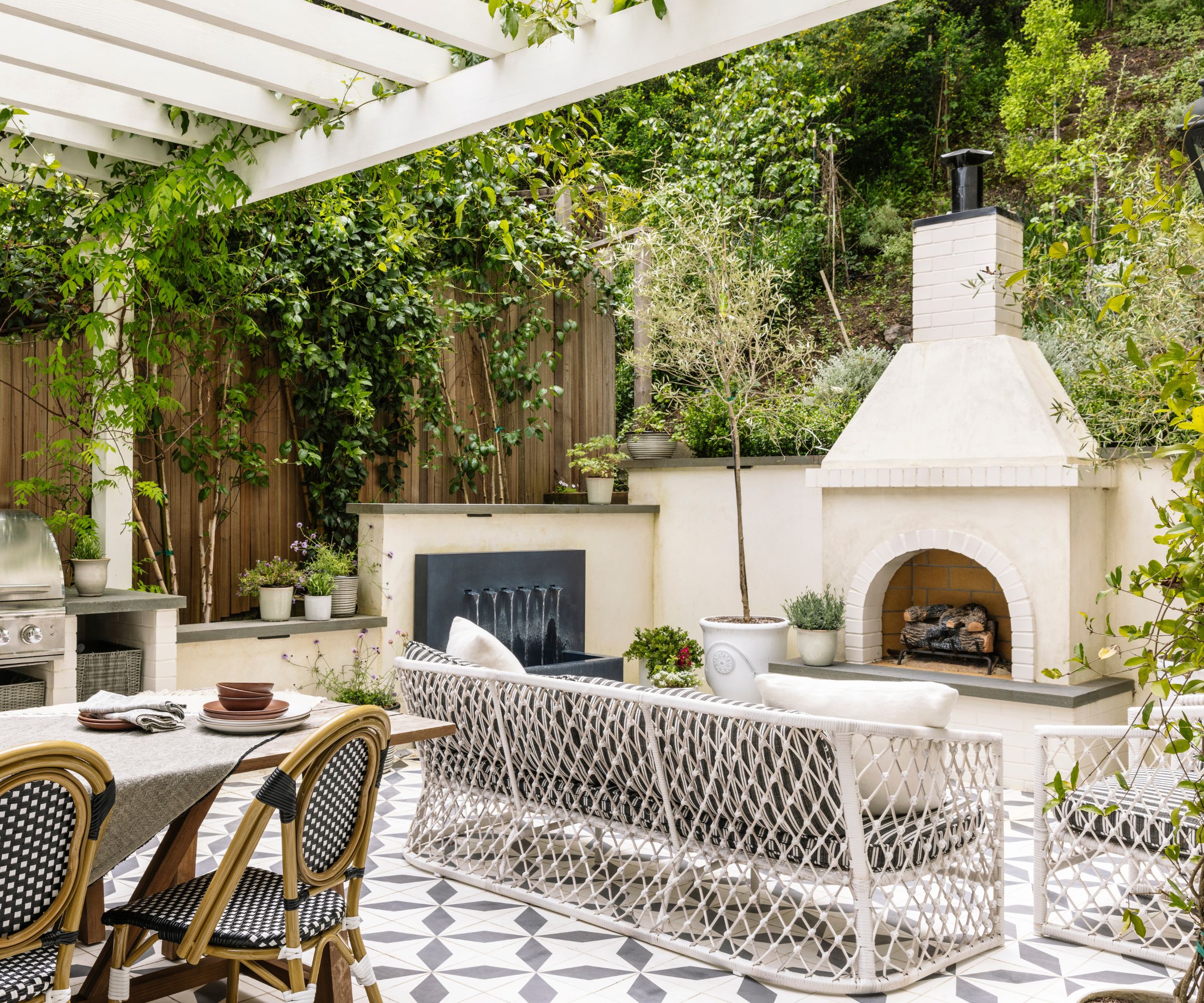 An outdoor living area with a large fireplace, patterned floor tiles, a water feature, and furniture with a knotted design