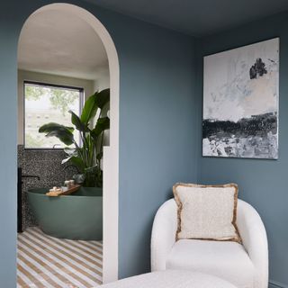 view into an ensuite with striped flooring and a green bath from an open archway showing a cream armchair in the foreground