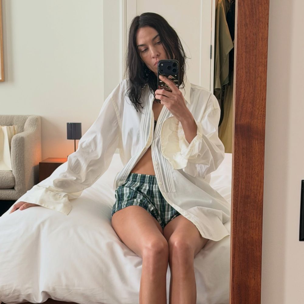Alexa Chung takes a mirror selfie wearing boxer shorts with a white skirt and black mule bow heels.