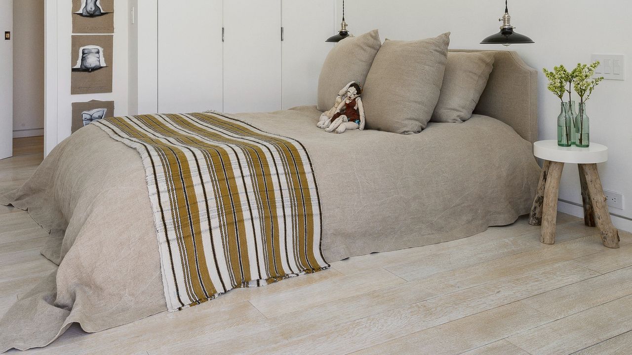 A bedroom with a bed dressed in beige linen with pendant lights on either side