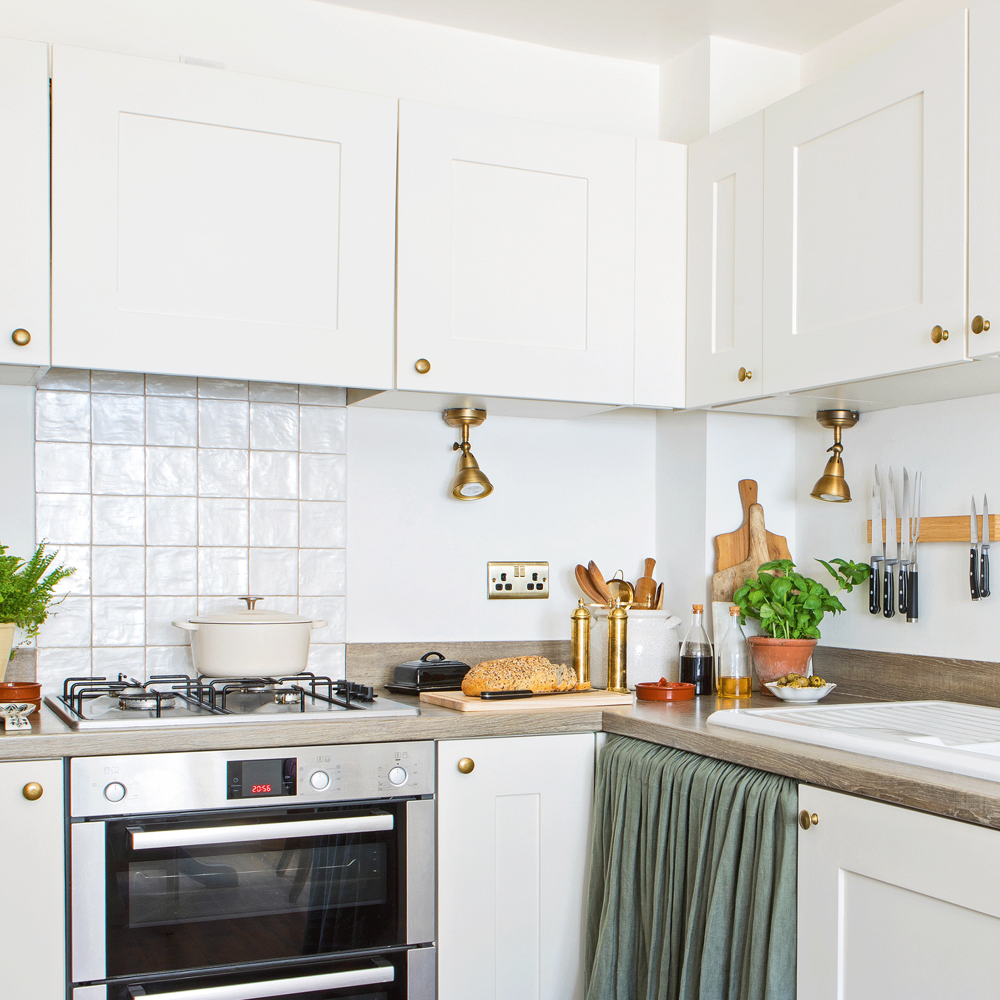 White kitchen with copper under cabinet lights, green kitchen skirts and white cast iron pot on hob