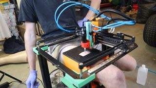 A still from a YouTube video showing a 3D printer frame over the top of someone's leg, giving them a tattoo with the attached gun.