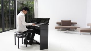 Man sits behind a Roland digital piano in a white room