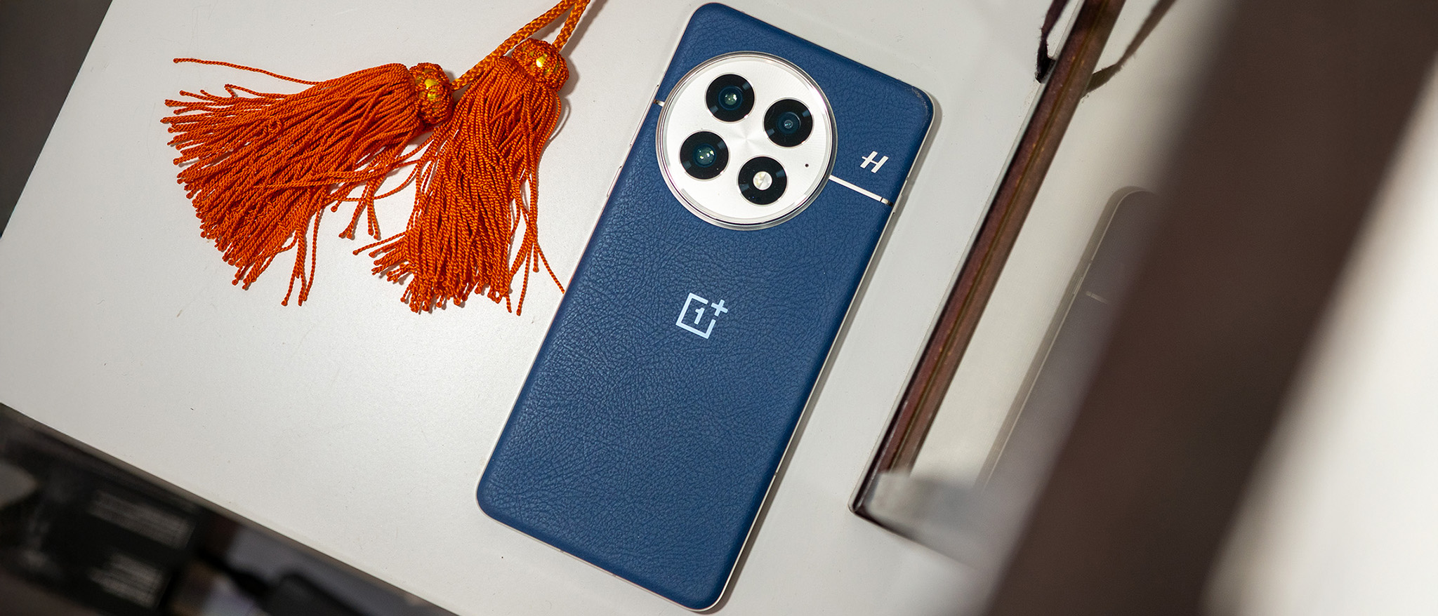 The back of the blue OnePlus 13 next to some orange tassels
