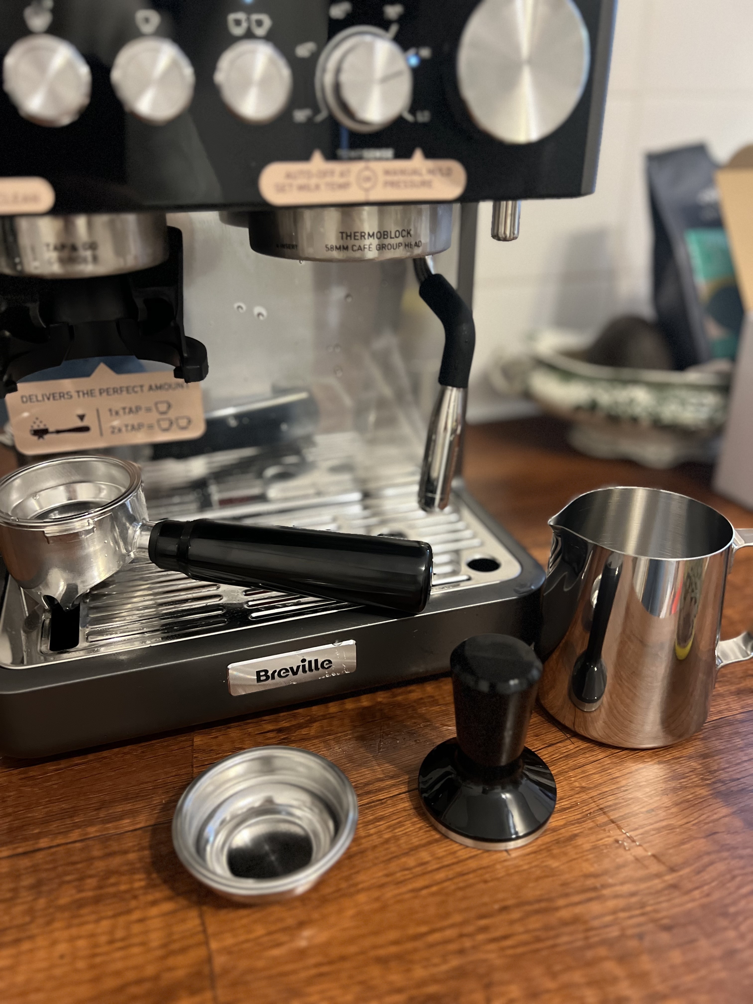 Close-up image of the Breville Barista Sense Espresso Machine in gray and black with all of the coffee accessories around it like the milk jug, tamper, and portafiller.
