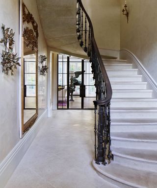Winding stone staircase with ornate black metal bannisters and stone floor with mirror on wall of hallway