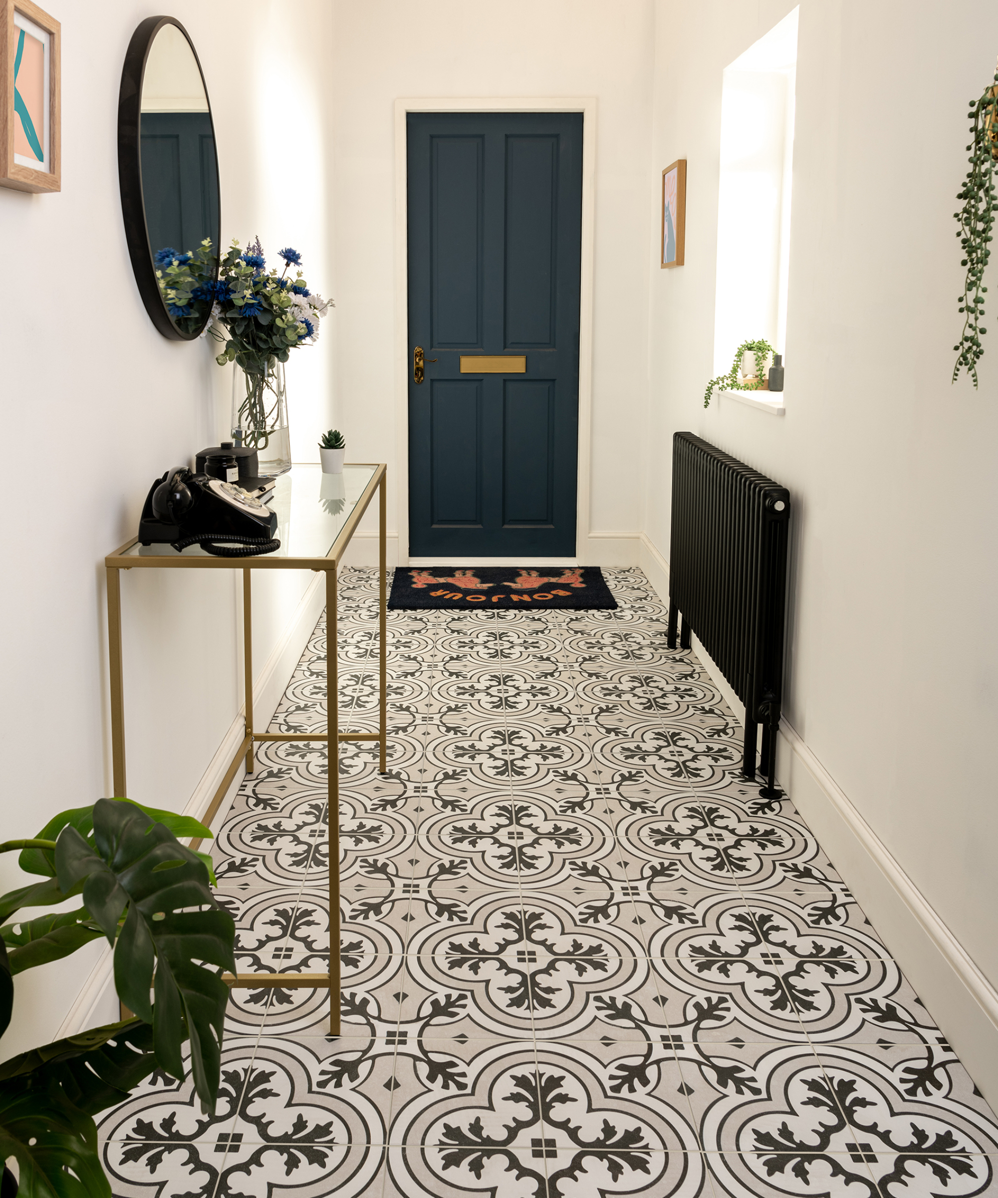 narrow hallway with black and white tiled floor, white walls, black radiator, dark blue front door, slim gold and glass console table with mirror above