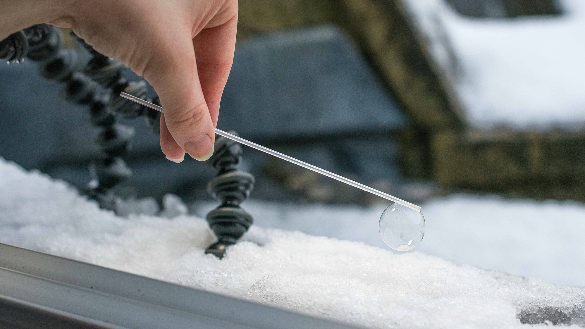 Bubble on the end of a straw, being placed on a snow-covered window sill