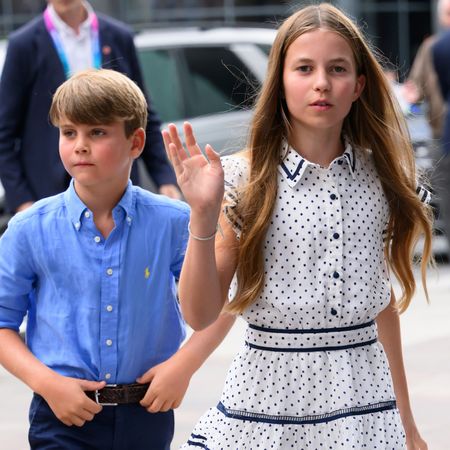 Princess Charlotte waving in a white dress walking in front of Prince Louis