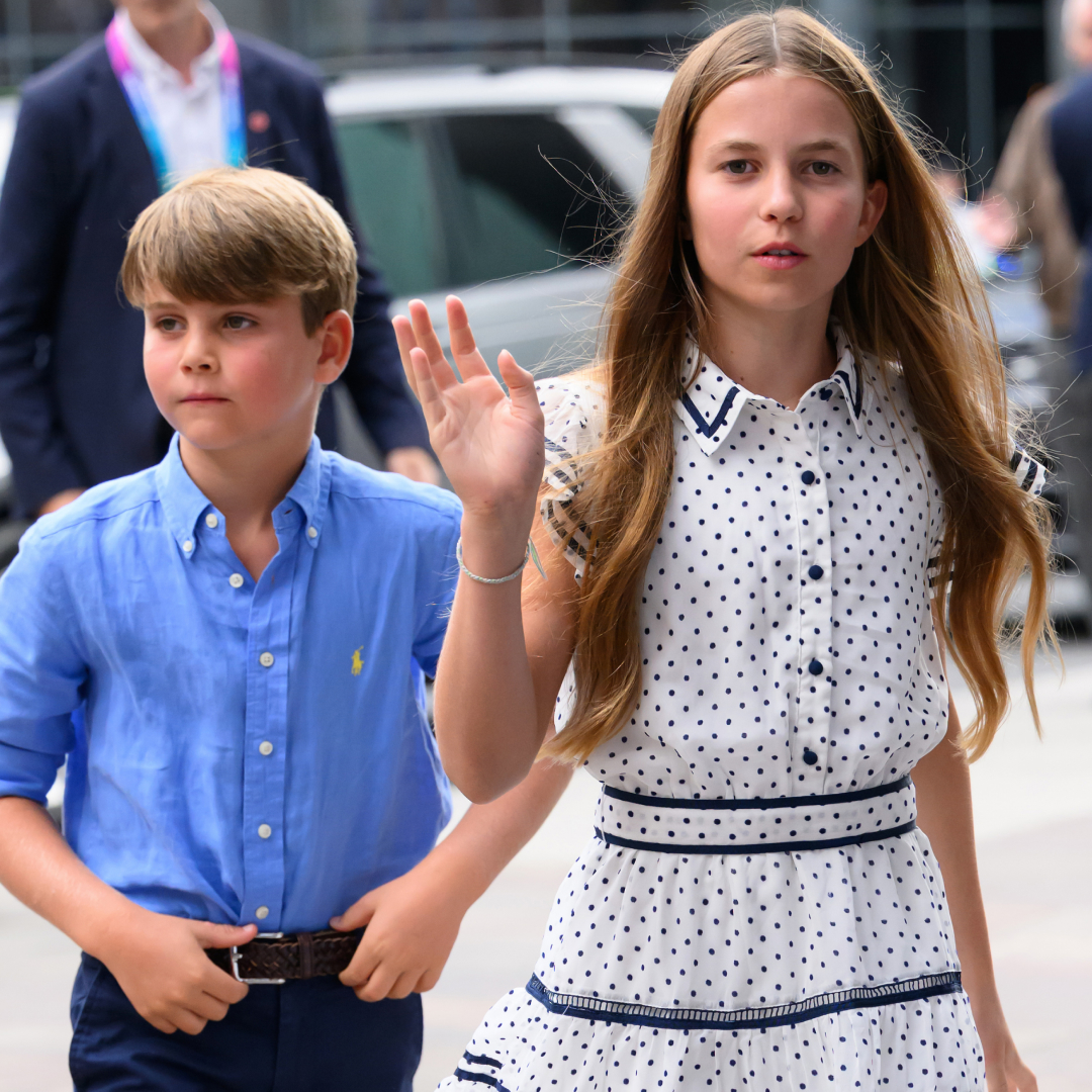 Princess Charlotte waving in a white dress walking in front of Prince Louis