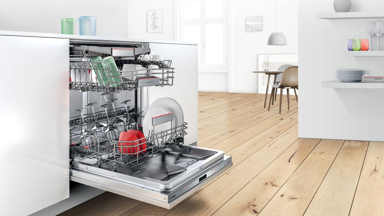 eco-friendly dishwasher tablets being used in a built-in dishwasher, in a white modern kitchen with a wooden floor, dining set, and plates and glasses on floating shelves