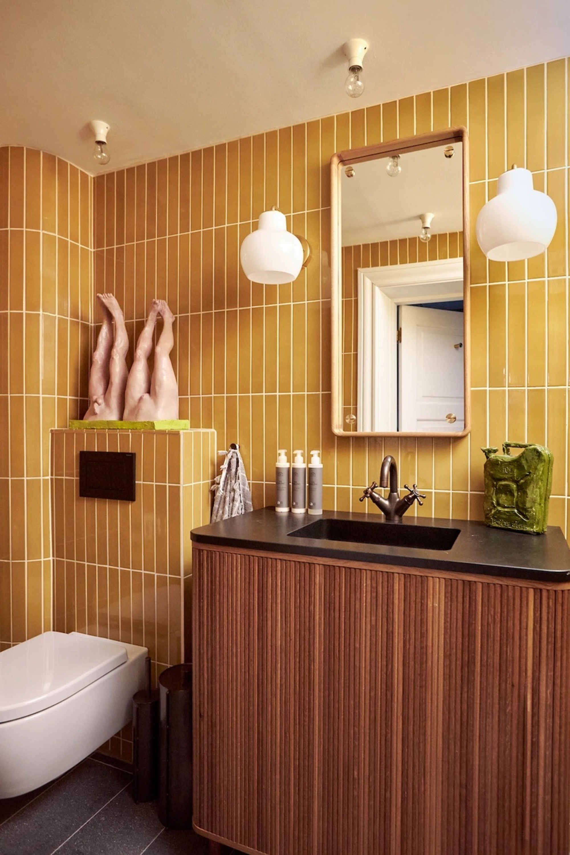 yellow bathroom with wall sconces either side of the mirror hung above a fluted timber vanity with black counter