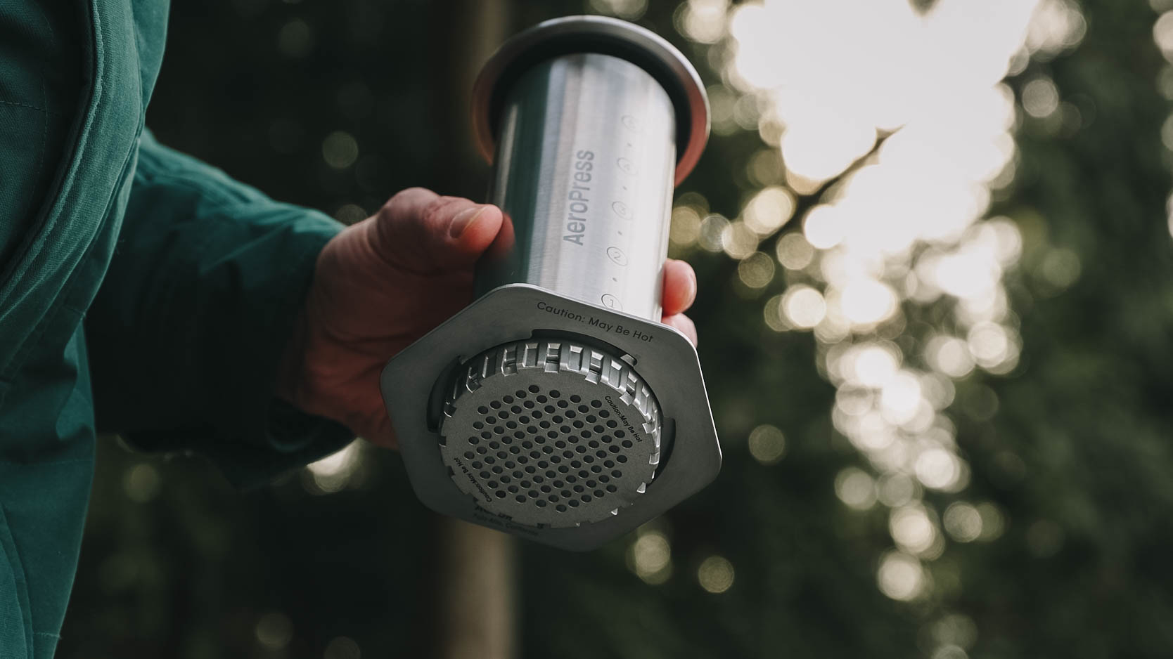 Man holding steel AeroPress coffee maker outdoors