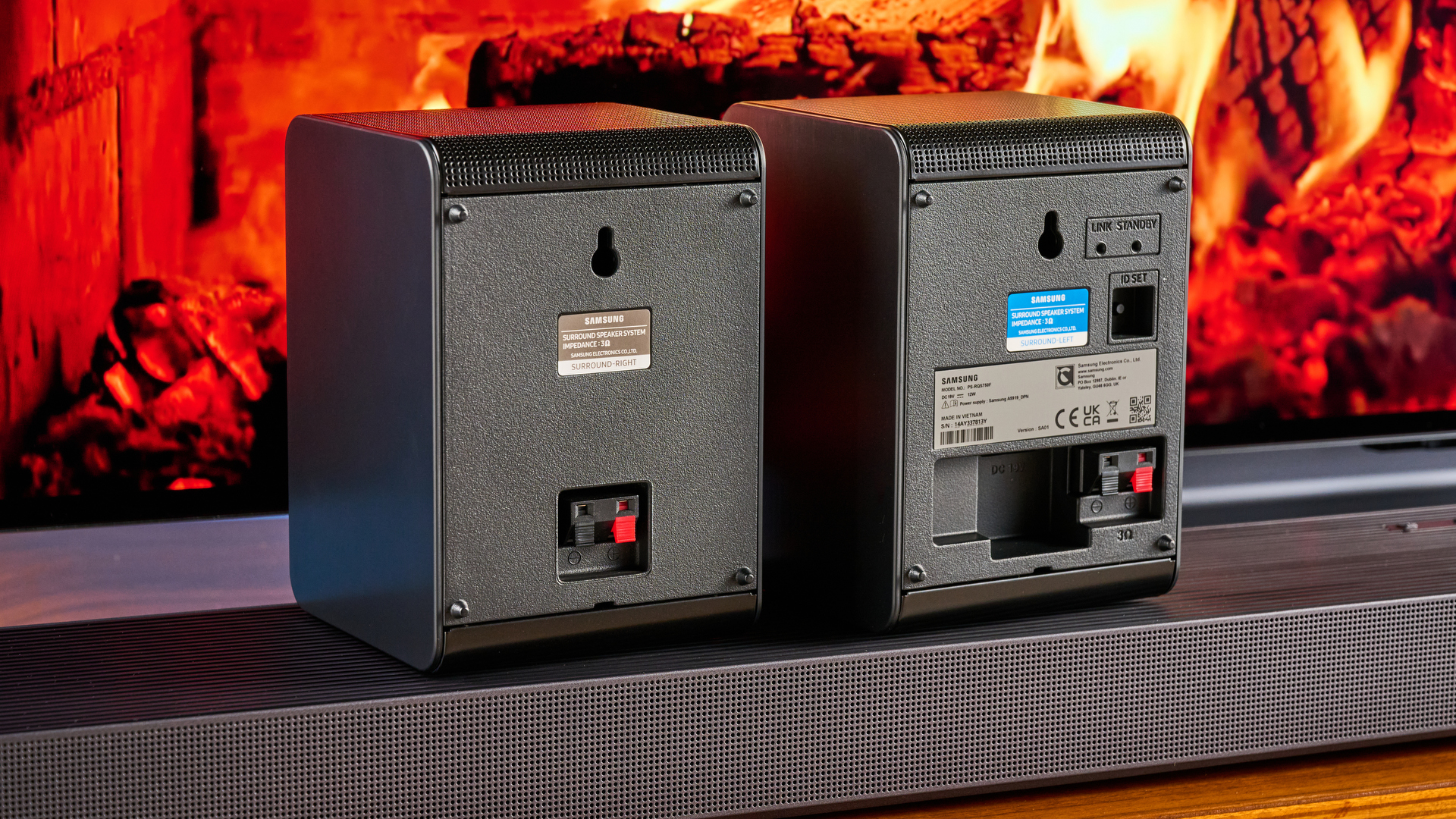 the samsung qs750f soundbar with two rear surround speakers and subwoofer photographed against a blue background and a TV