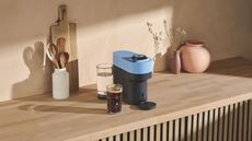 Image of a blue Nespresso Vertuo POp on a wooden counter in a minimalist kitchen.