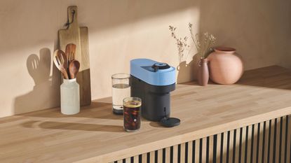 Image of a blue Nespresso Vertuo POp on a wooden counter in a minimalist kitchen.