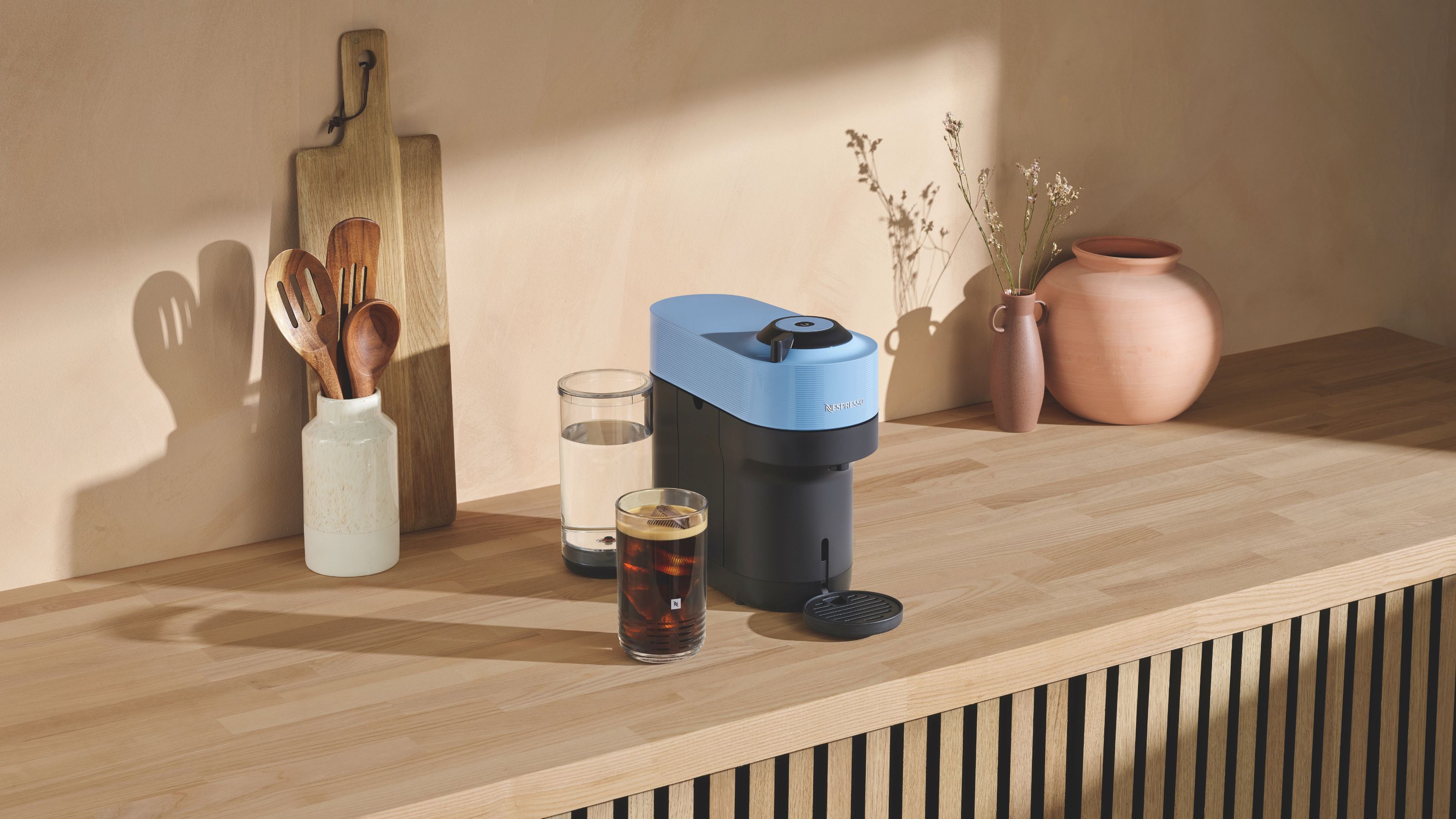 Image of a blue Nespresso Vertuo POp on a wooden counter in a minimalist kitchen.