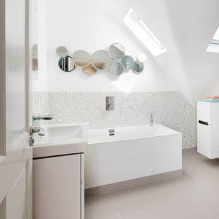 white bathroom with sloping ceiling and skylights, with a minimalist bath and and round wall mirrors