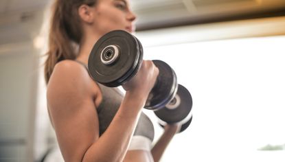 Fit young woman doing bicep curls with dumbbells