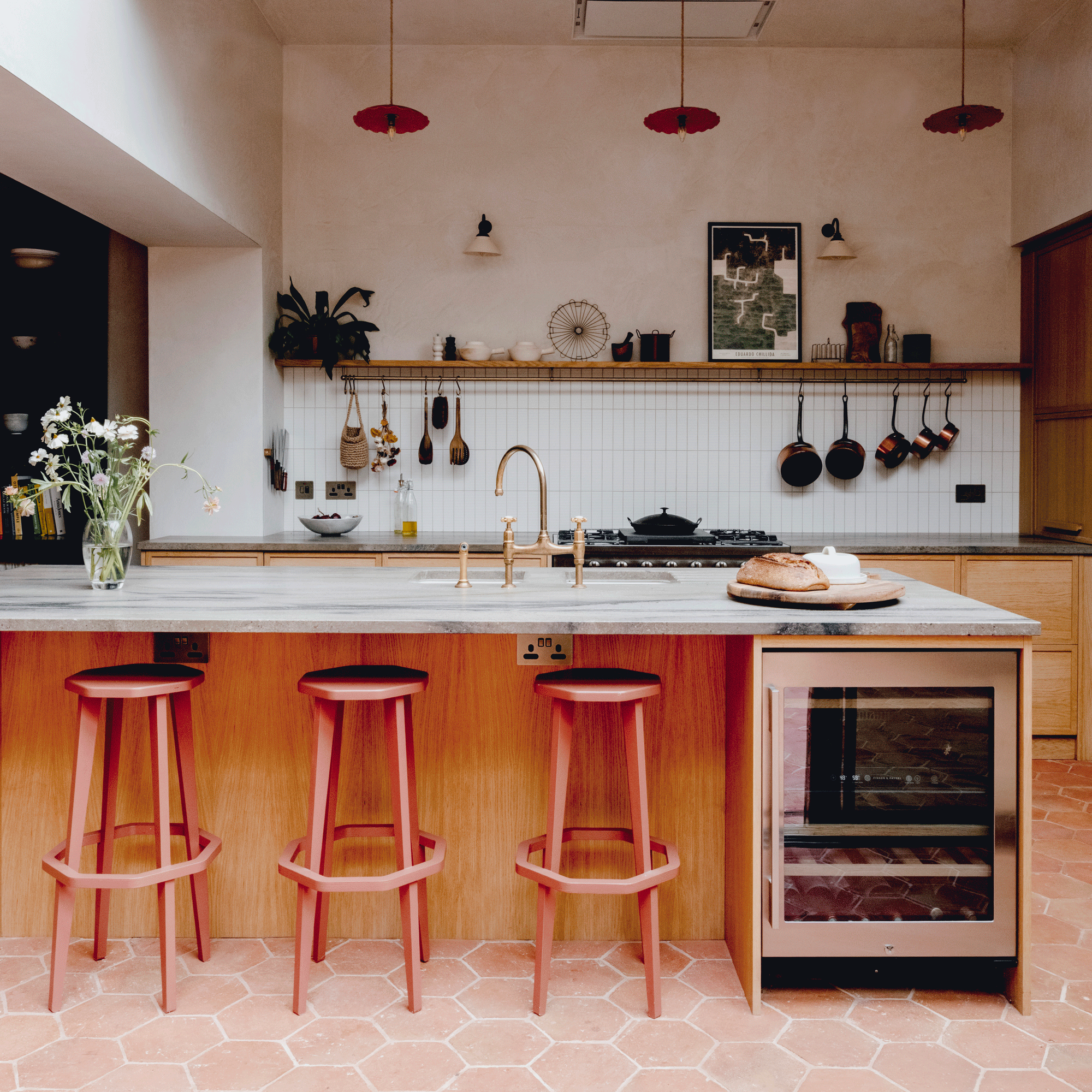 an open plan kitchen with terracotta floor tiles and a large kitchen island with a marble countertop and pink bar stools
