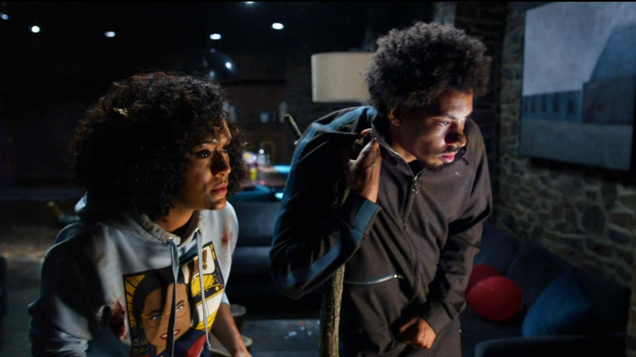 Melvin Gregg and Grace Byers looking at a TV in The Blackening.