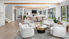 A large open plan living space with a neutral color palette, white arm chairs around a coffee table in the foreground, and a dining space in the background