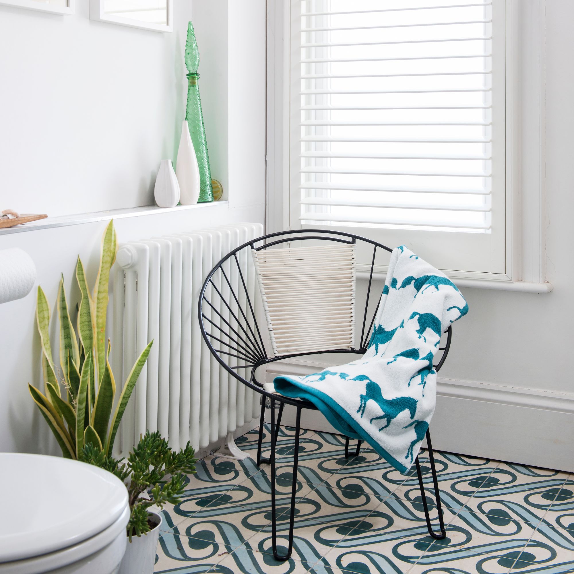 An open back black chair in a blue and white bathroom, next to two houseplants