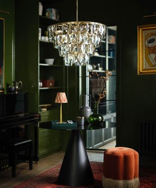 glass chandelier hanging over decorative table with cone base and glass top in room with dark green walls