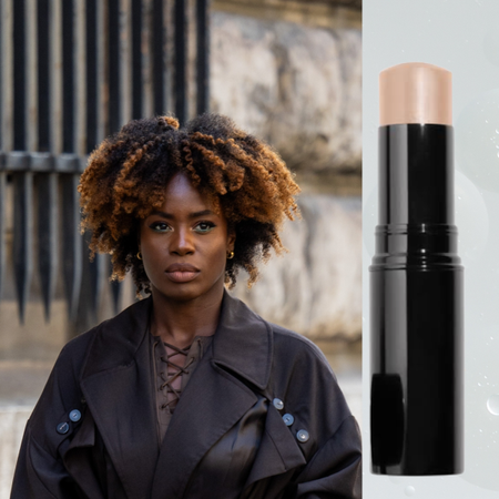 A woman wearing a black trench coat over a brown dress. She is next to a beauty product on sale.