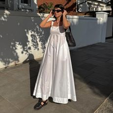 Woman on street wears white dress, fisherman sandals and woven bag
