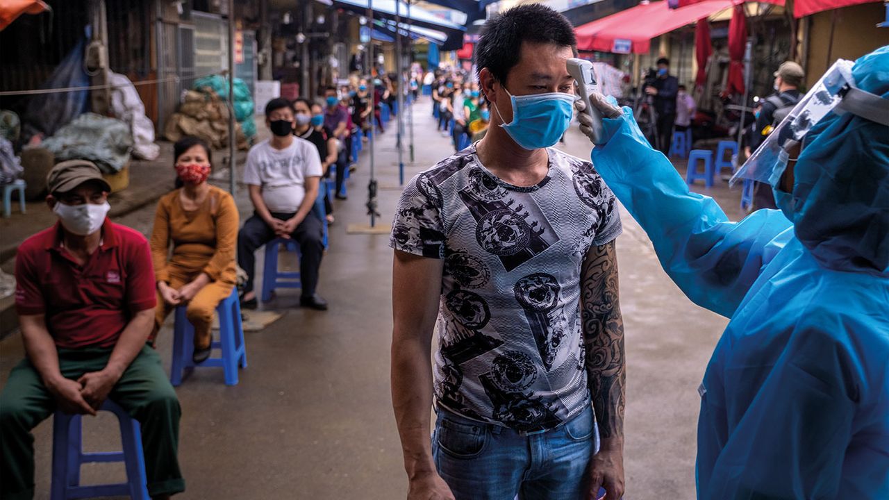 Health worker taking market trader&amp;#039;s temperature in Vietnam © Linh Pham/Getty Images