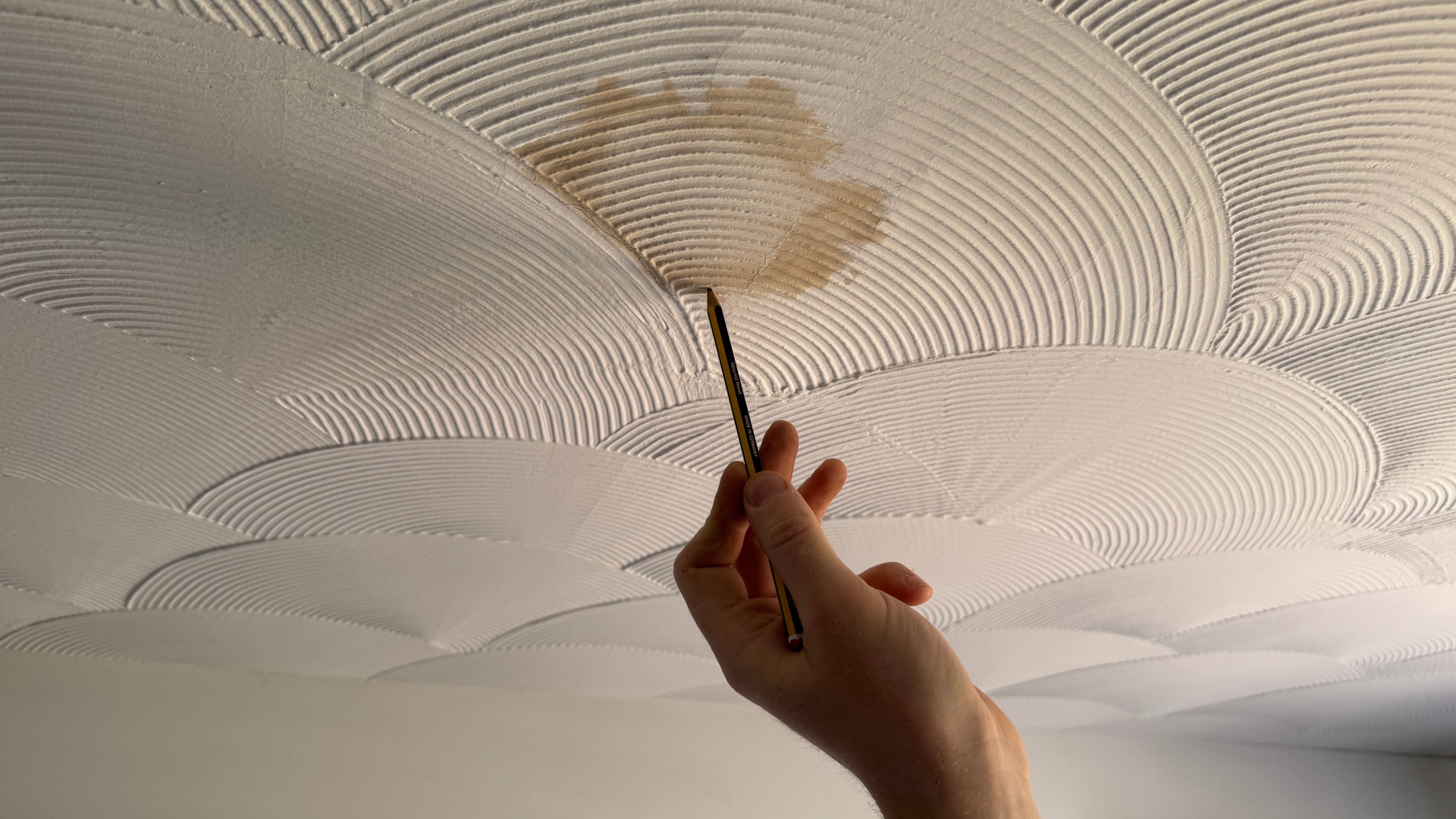Drawing a pencil line around a damp patch on the ceiling