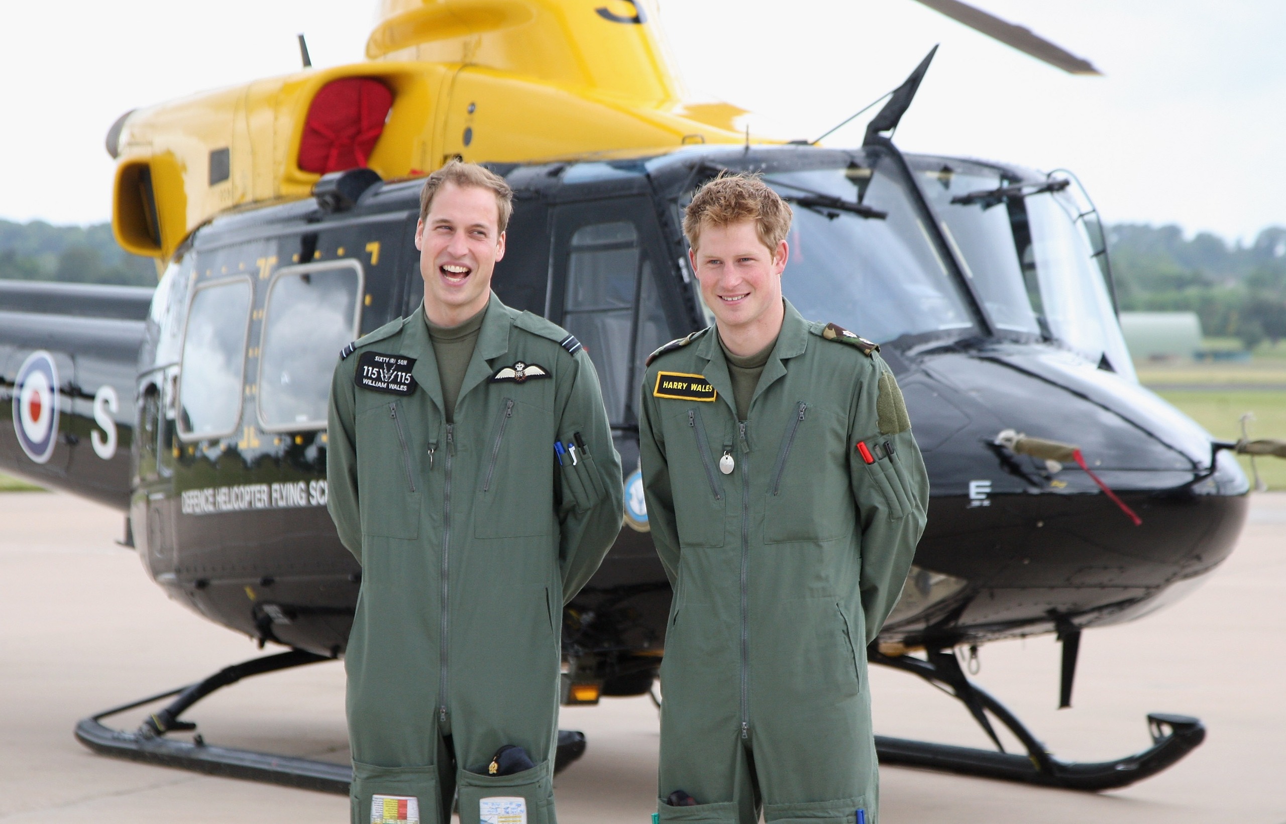 Prince William and Prince Harry smiling in front of a helicopter