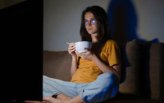 A woman watching TV and eating a bowl of cereal in the dark