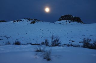 a bright moon over snow-covered hills
