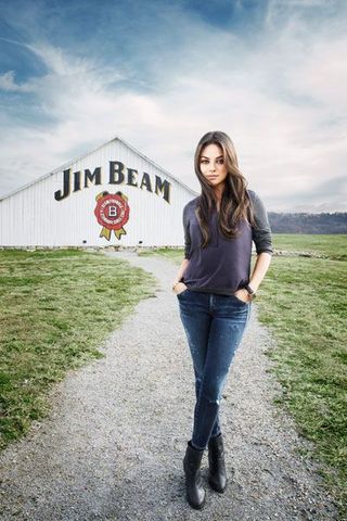 Mila Kunis posing on gravel path, in front of Jim Bean barn