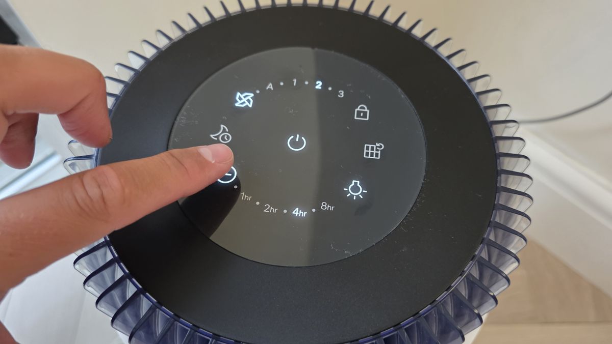 A man's finger presses the timer button on top of the Coway Airmega 100.