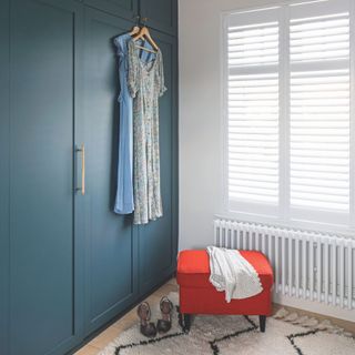 White dressing room with blue fitted wardrobes, a red stool, and a cream rug