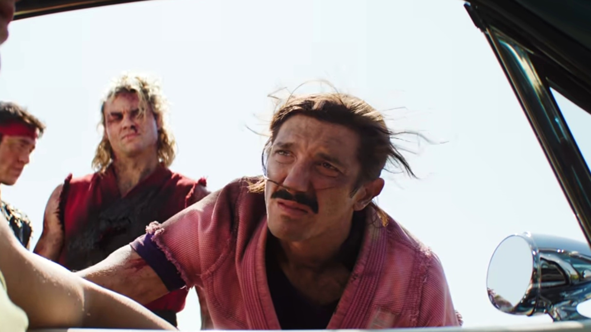 Andrew Schulz leaning into a car window as Dan Hibiki in Street Fighter