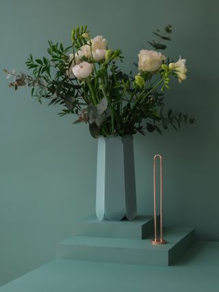 A bouquet of flowers in a sage green vase next to a copper stem insert