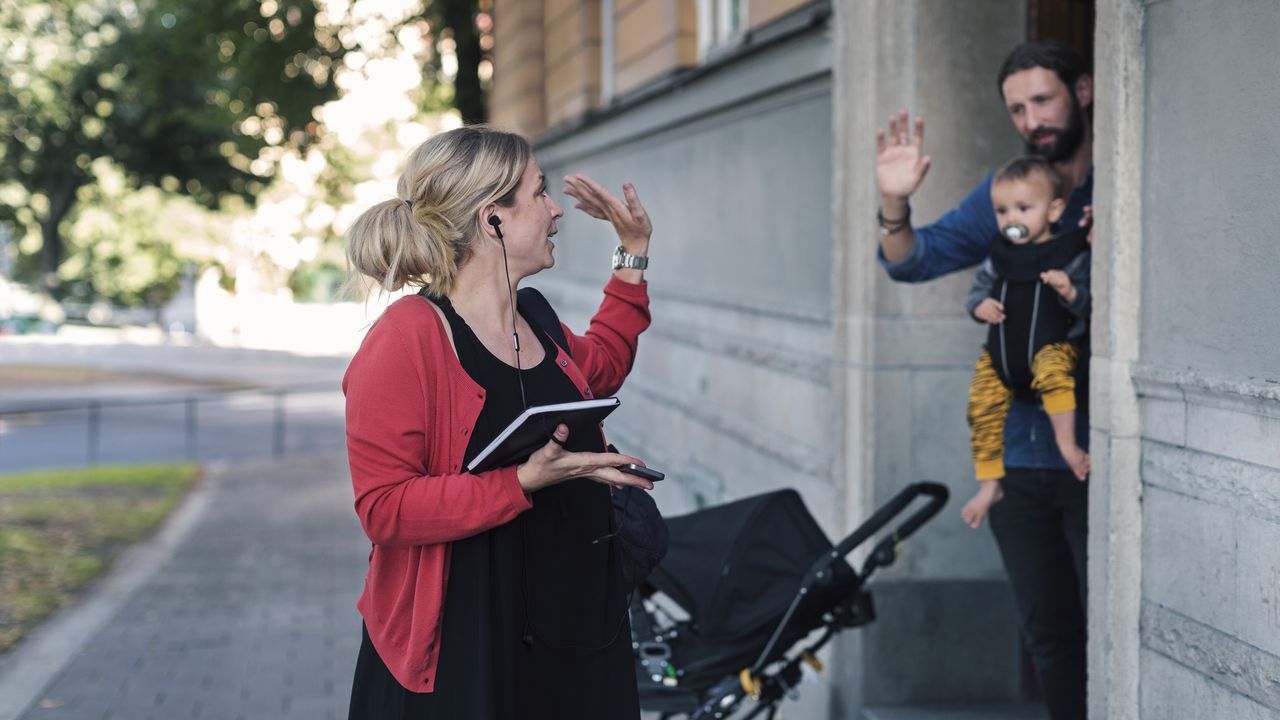 A man in a business clothes waves goodbye to her husband and child as she heads to work.