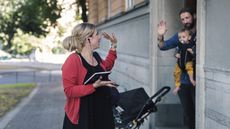 A man in a business clothes waves goodbye to her husband and child as she heads to work.