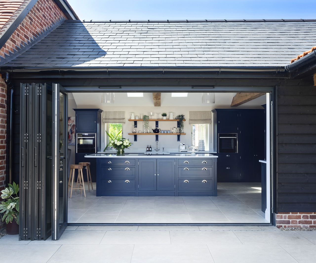 A view into a single-storey kitchen space with bifold doors and Shaker-style navy kitchen