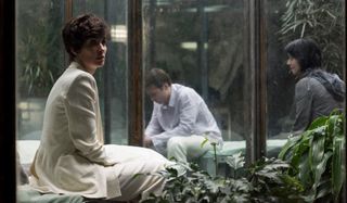 The OA Paz Vega sitting in a greenhouse, dressed in a white suit